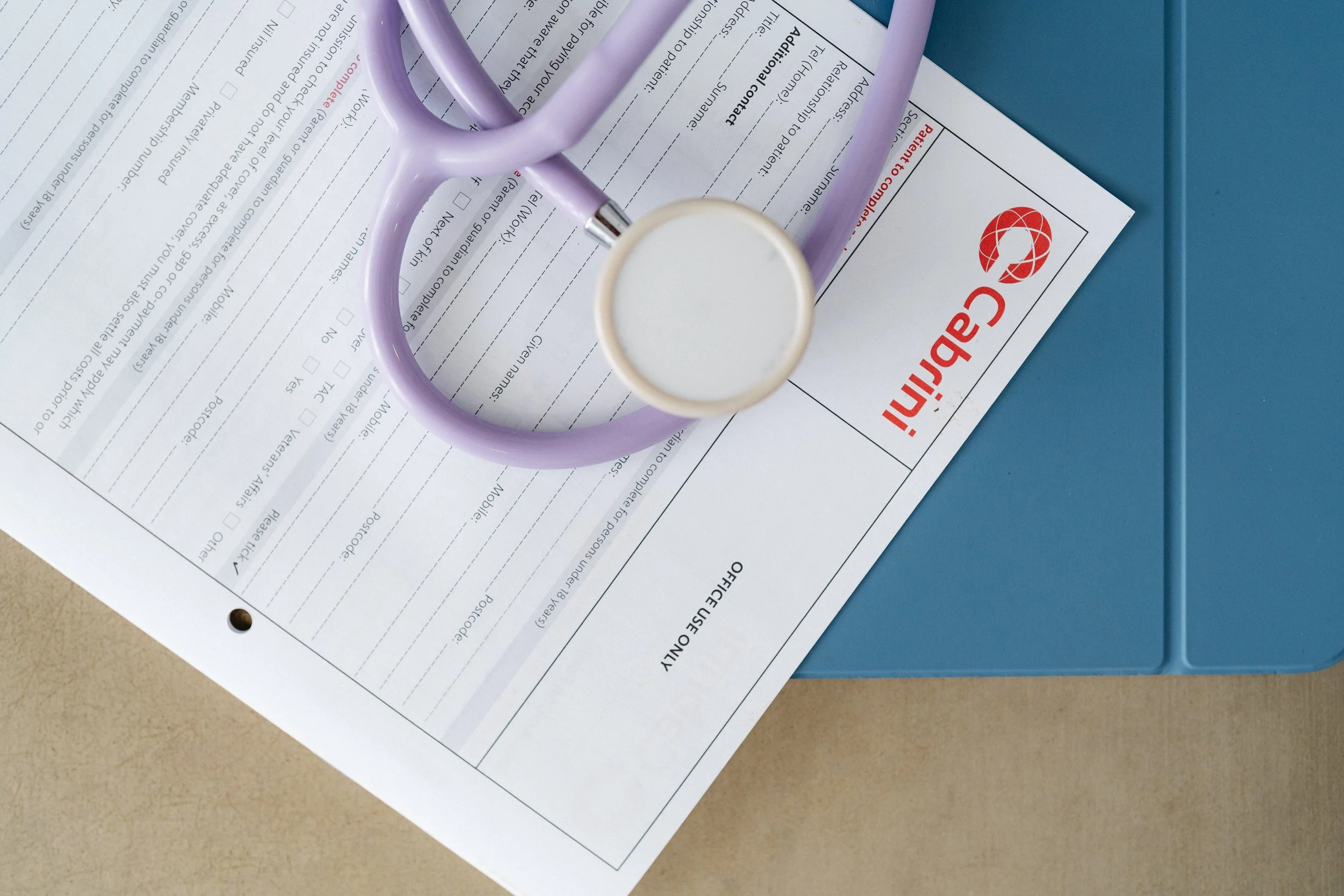 A lavender stethoscope resting on a medical form labeled 'Application for a Patient to Do Practice' in red and black text, on a blue surface.
