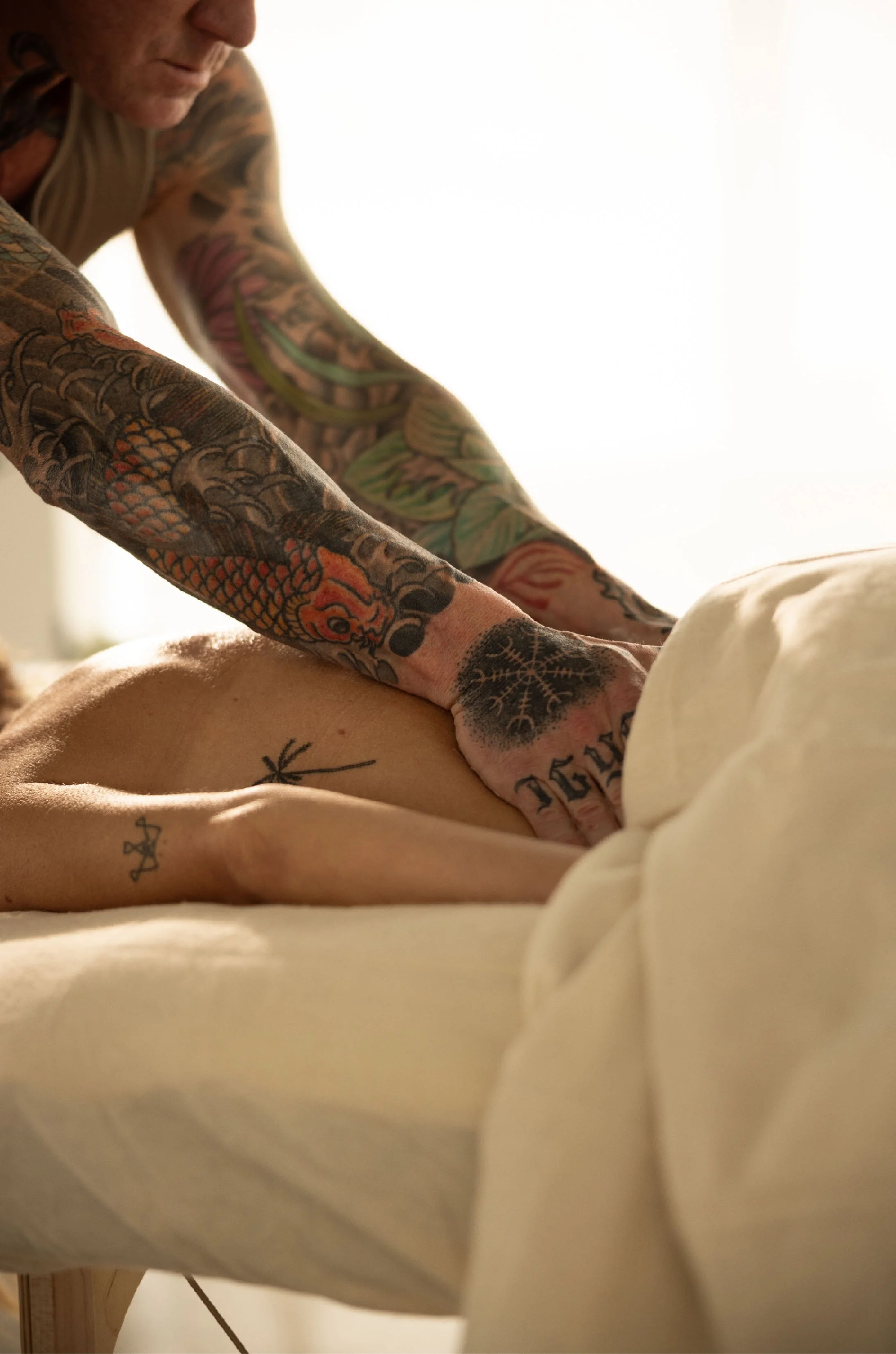 A person giving a massage to another person in a setting with a cream-colored bed and soft lighting.