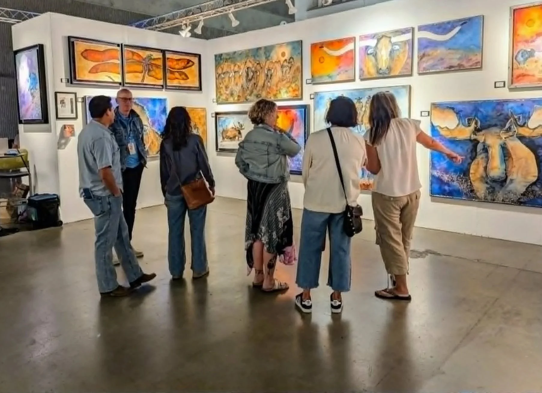 Group of people inside an art gallery looking at colorful paintings on the wall, including animals and abstract designs.