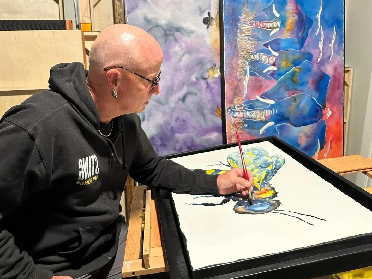 Peter painting with a small detail brush on a large, colorful canvas in an art studio.