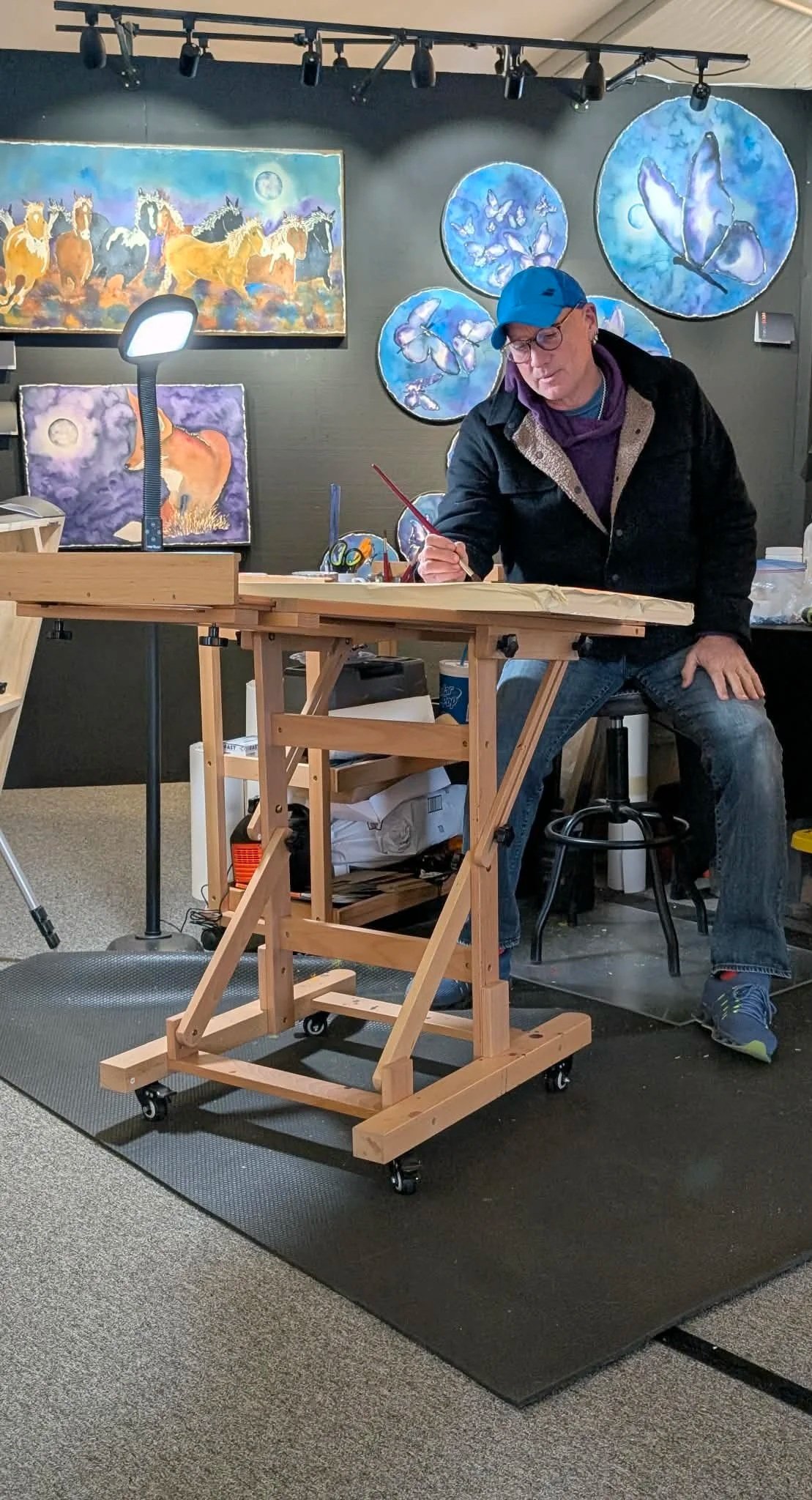 Peter creating on a wooden table in an art studio with paintings of horses and butterflies on the wall.