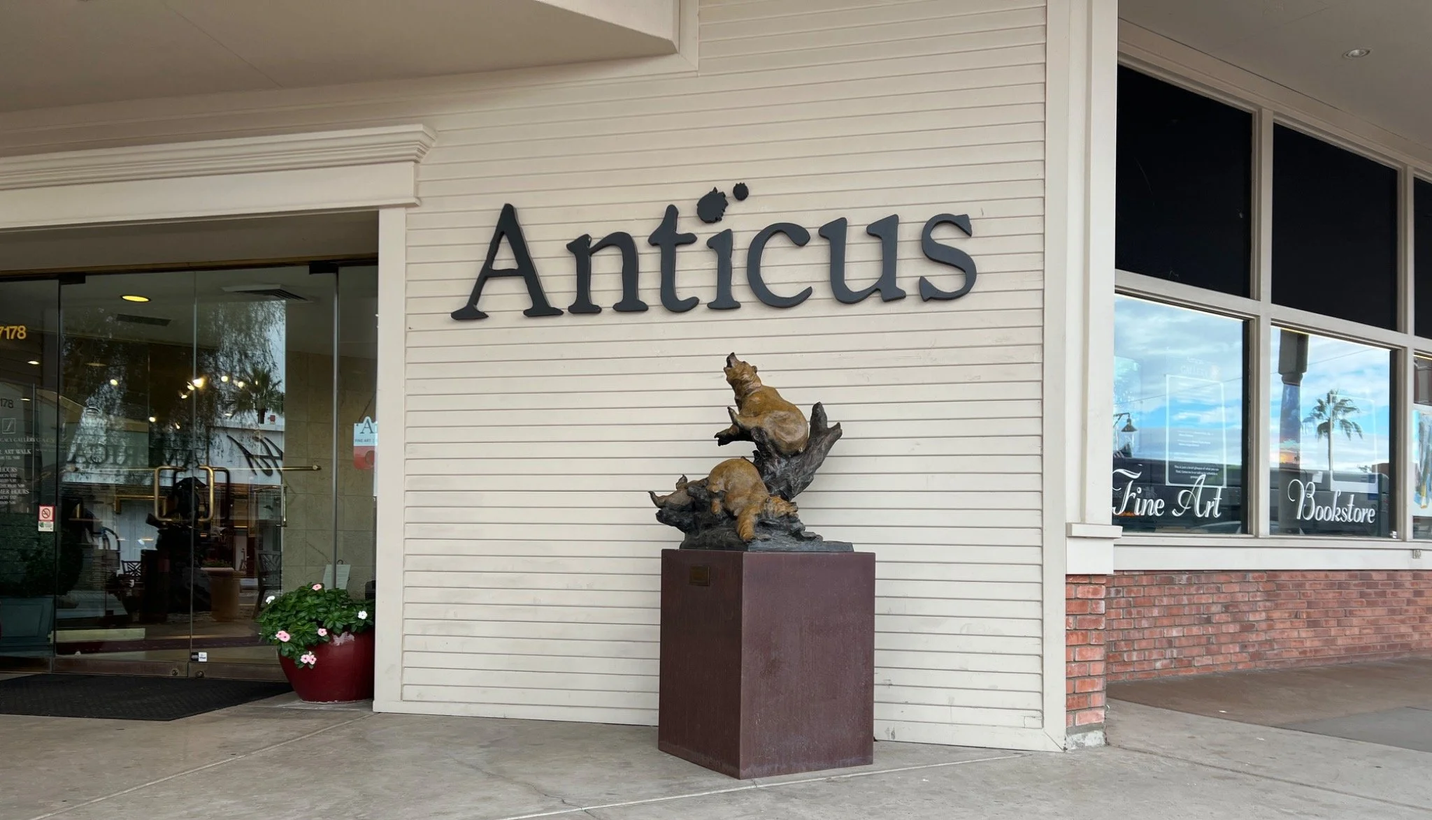 Exterior view of Anticus art gallery, featuring a bronze sculpture of dogs on a pedestal and a large sign with the gallery's name.