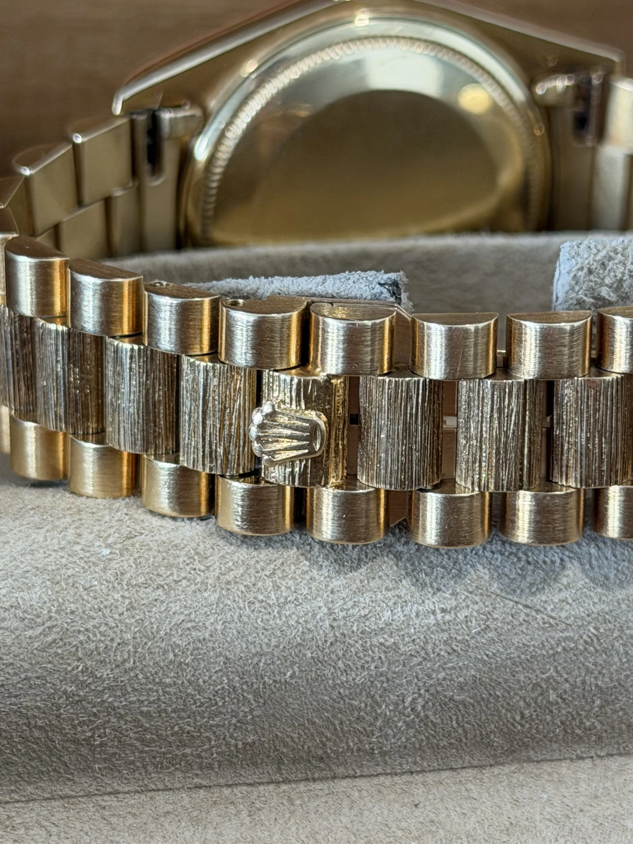 Close-up of a gold wristwatch with a metallic band and a textured face, resting on a beige textured surface.