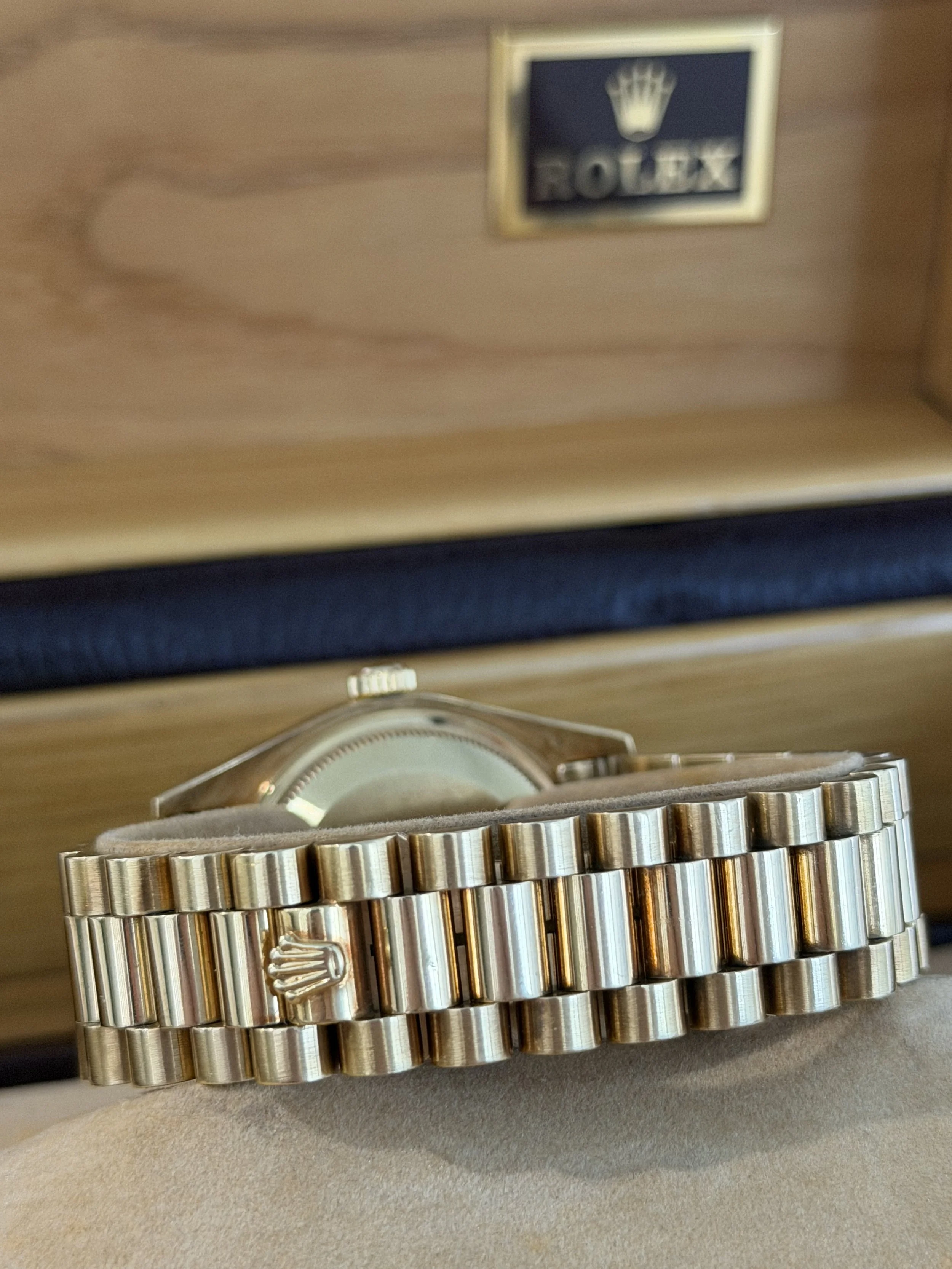 Close-up of a silver Rolex watch with a gold bracelet, placed on a surface with a beige background.