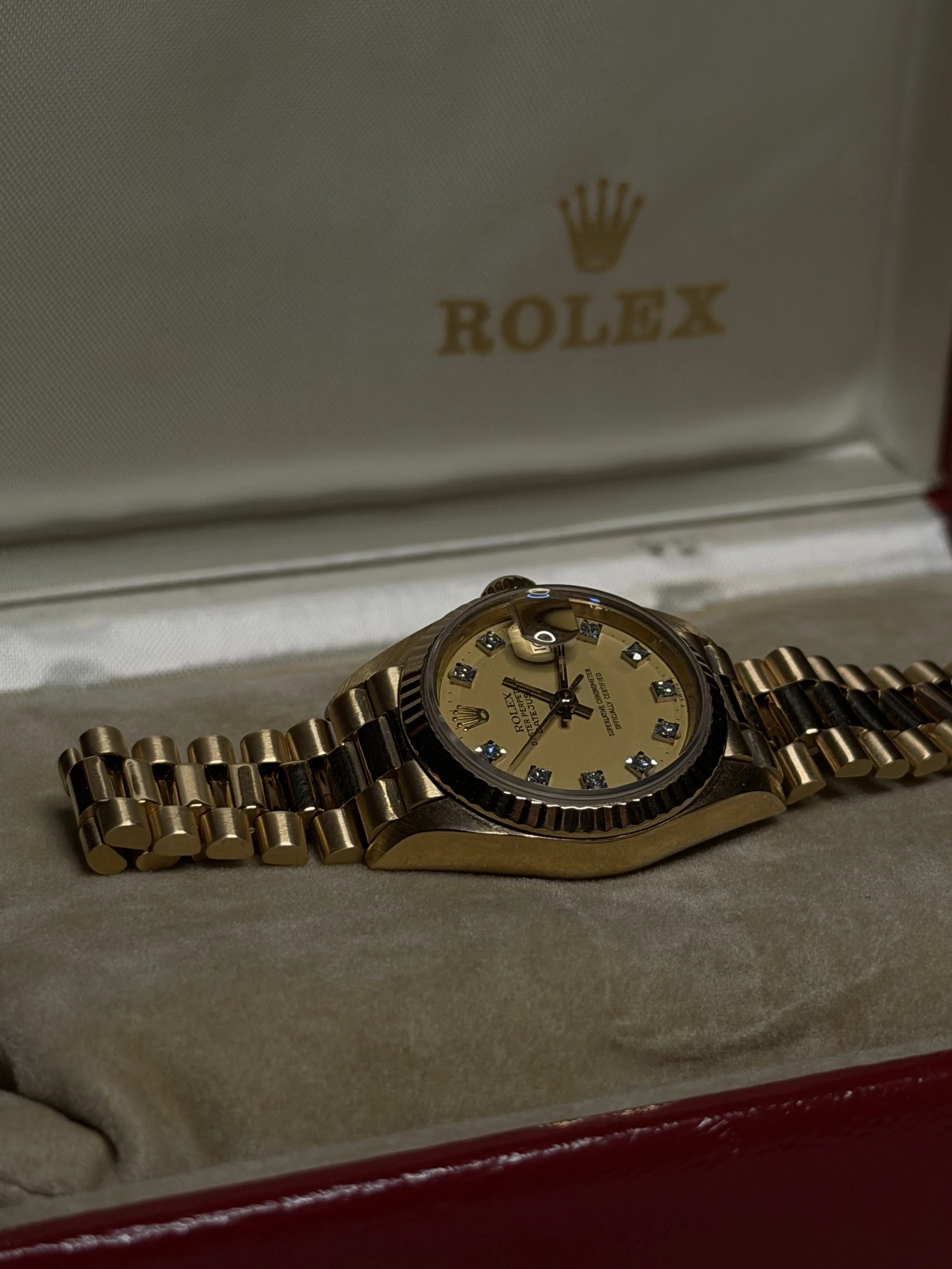 A gold Rolex watch with a gold band, showcased inside a white jewelry box with a padded interior. The Rolex logo is visible on the inside of the lid.