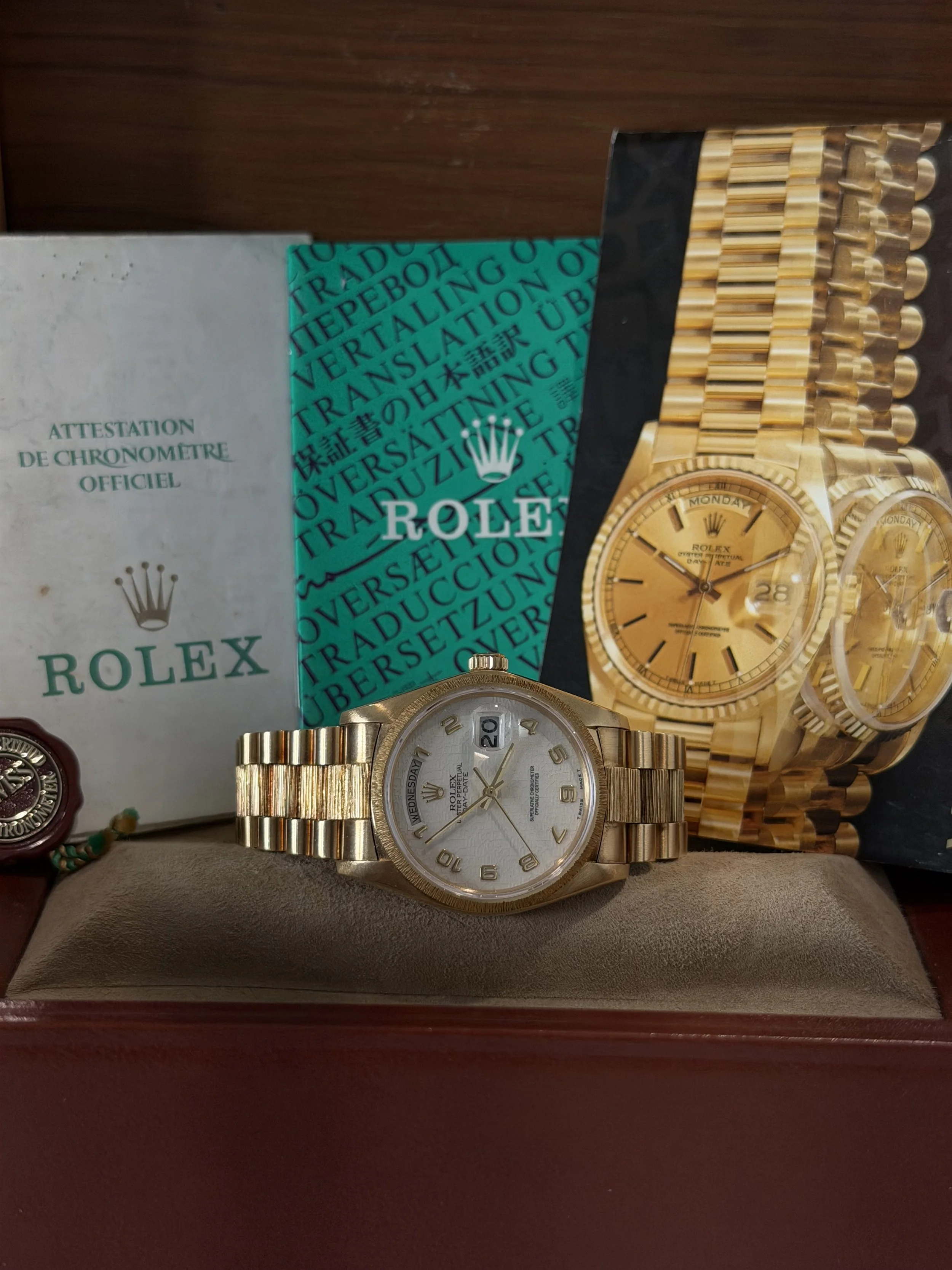 A gold Rolex watch with a white face and gold bracelet, a green paper with black text about Rolex, and a gold picture of a Rolex watch on a black background.