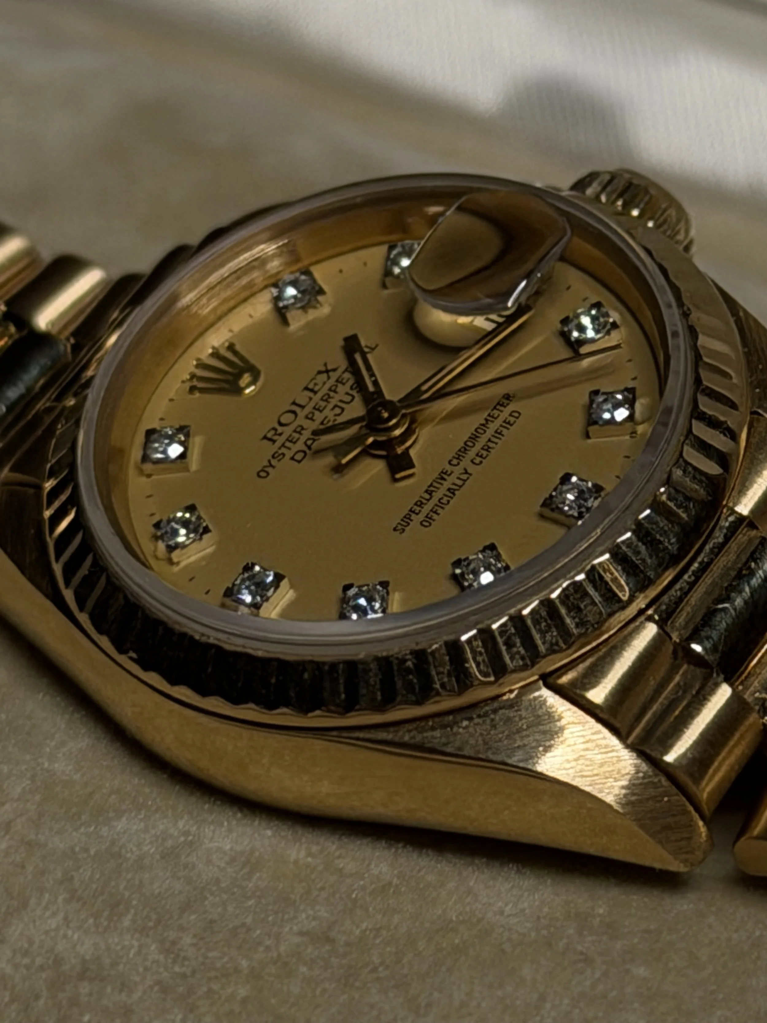 Close-up of a gold Rolex watch with diamond hour markers, a fluted bezel, and a champagne dial.