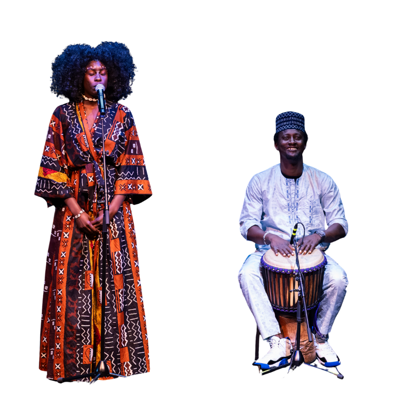 A woman in a patterned dress singing into a microphone and a man in traditional attire playing a drum on stage.