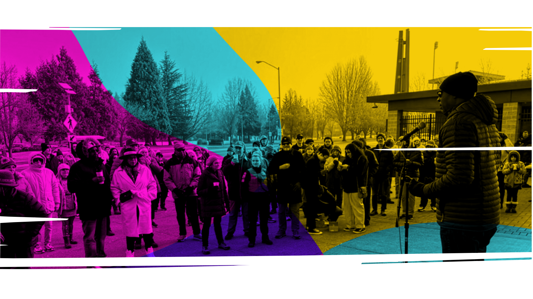 A group of people gathered outdoors in Eugene-Springfield, Oregon, listening to a speaker during a public event in a park-like setting with trees and a brick building in the background.