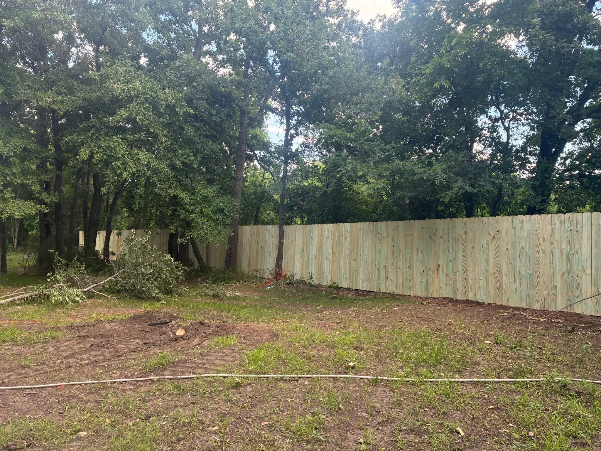 A backyard with a wooden privacy fence, trees, and a mix of grass and dirt on the ground.
