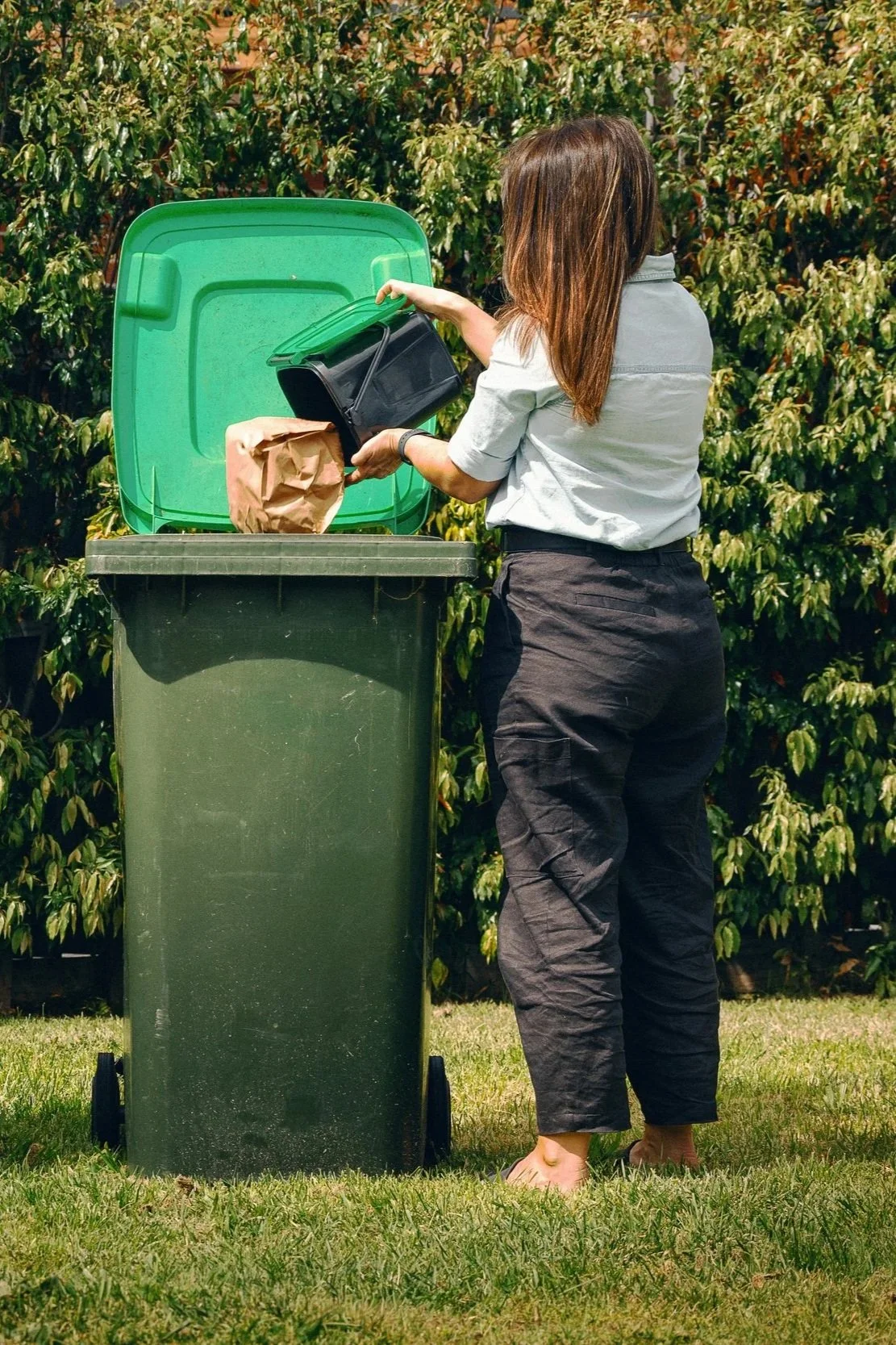 The Good Sort - Person emptying food scraps from a kitchen caddy into a green-lid FOGO bin.