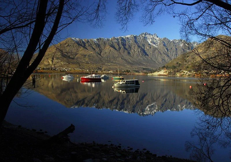 Boats floating on a calm lake with mountains in the background and trees framing the scene.