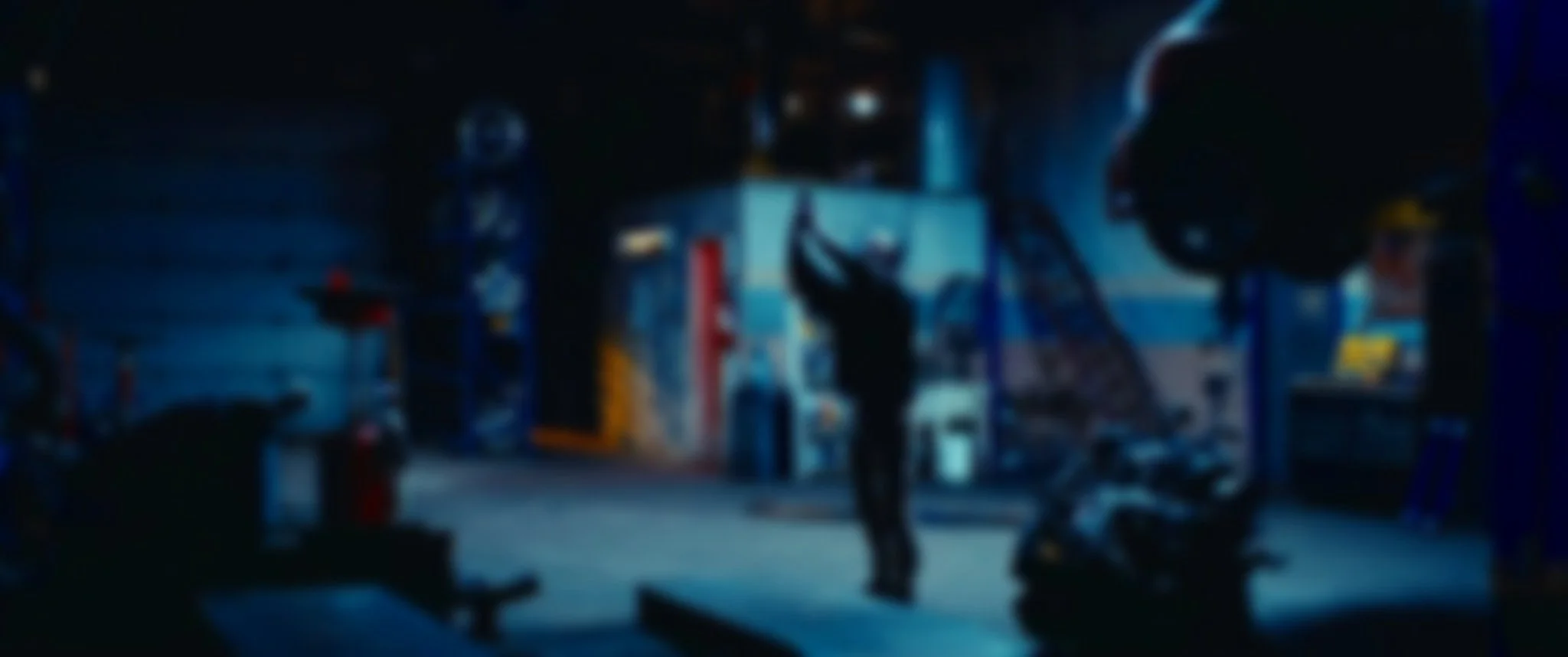 Un homme dans un garage ou atelier, levant un objet ou un outil, entouré de pneus, outils et équipements divers, dans une ambiance sombre.