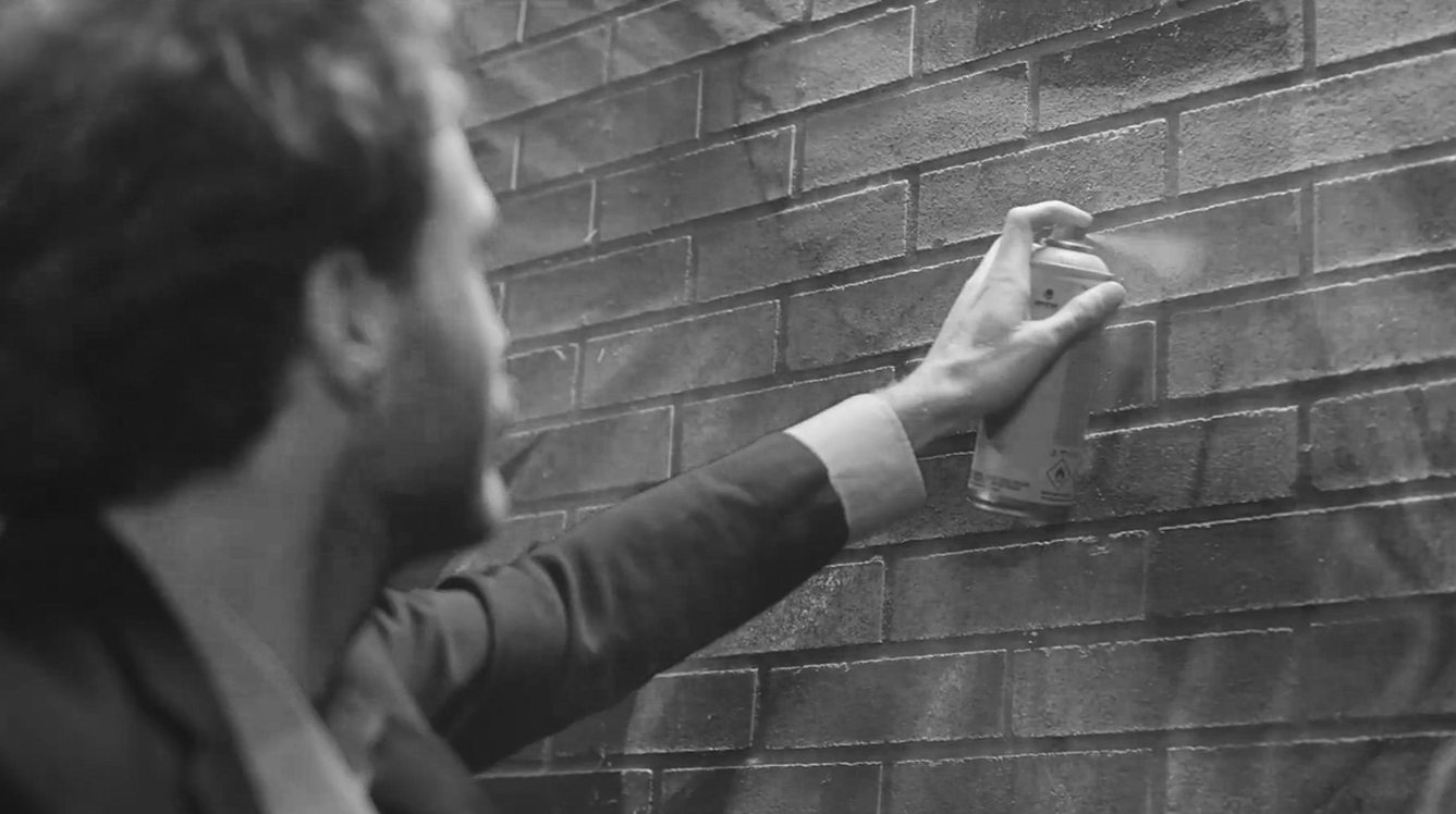 Une personne en costume utilise une bombe de peinture sur un mur en briques.