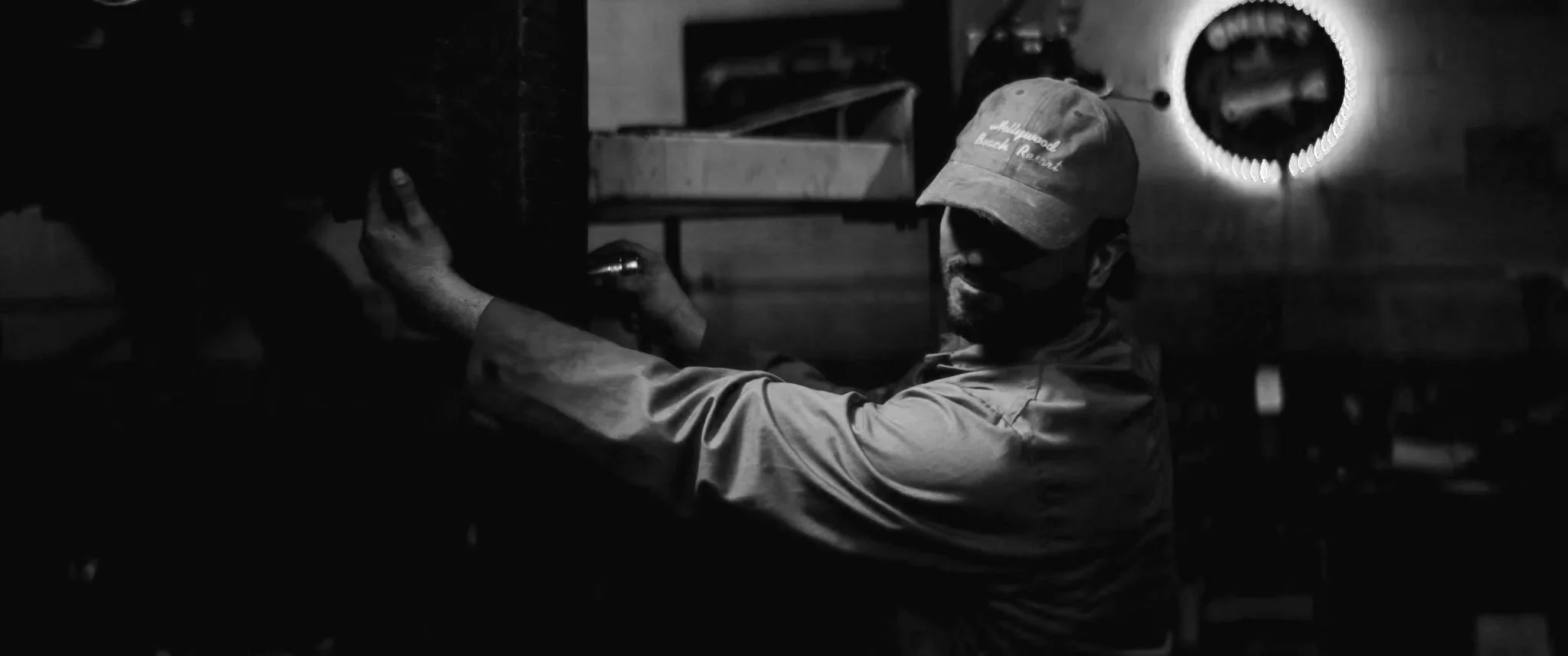 Un homme portant une casquette et un masque noir travaille sur une machine dans un environnement industriel sombre.