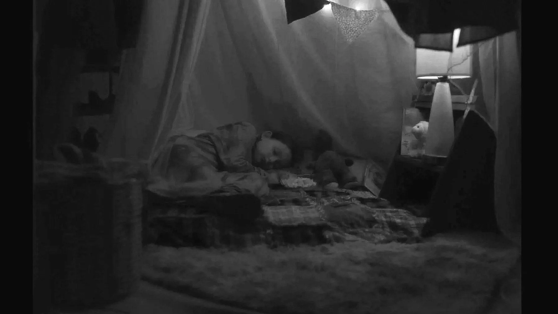 Personne dormant dans une tente, illuminated par une lampe, avec un poisson dans un aquarium à côté.