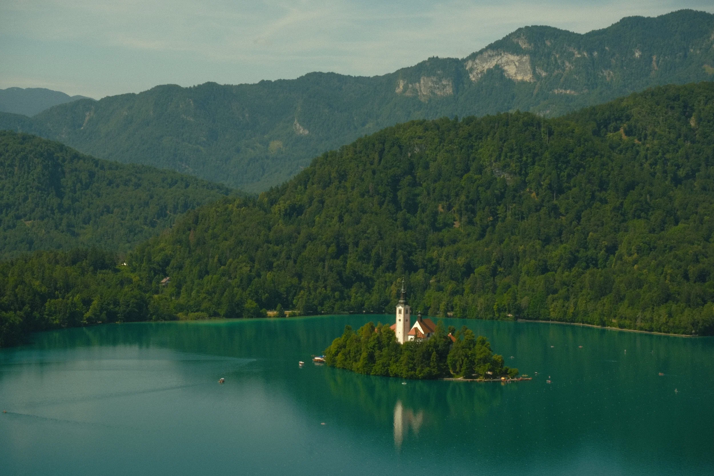 A serene lake surrounded by lush green mountains with a small church on the lakeshore.