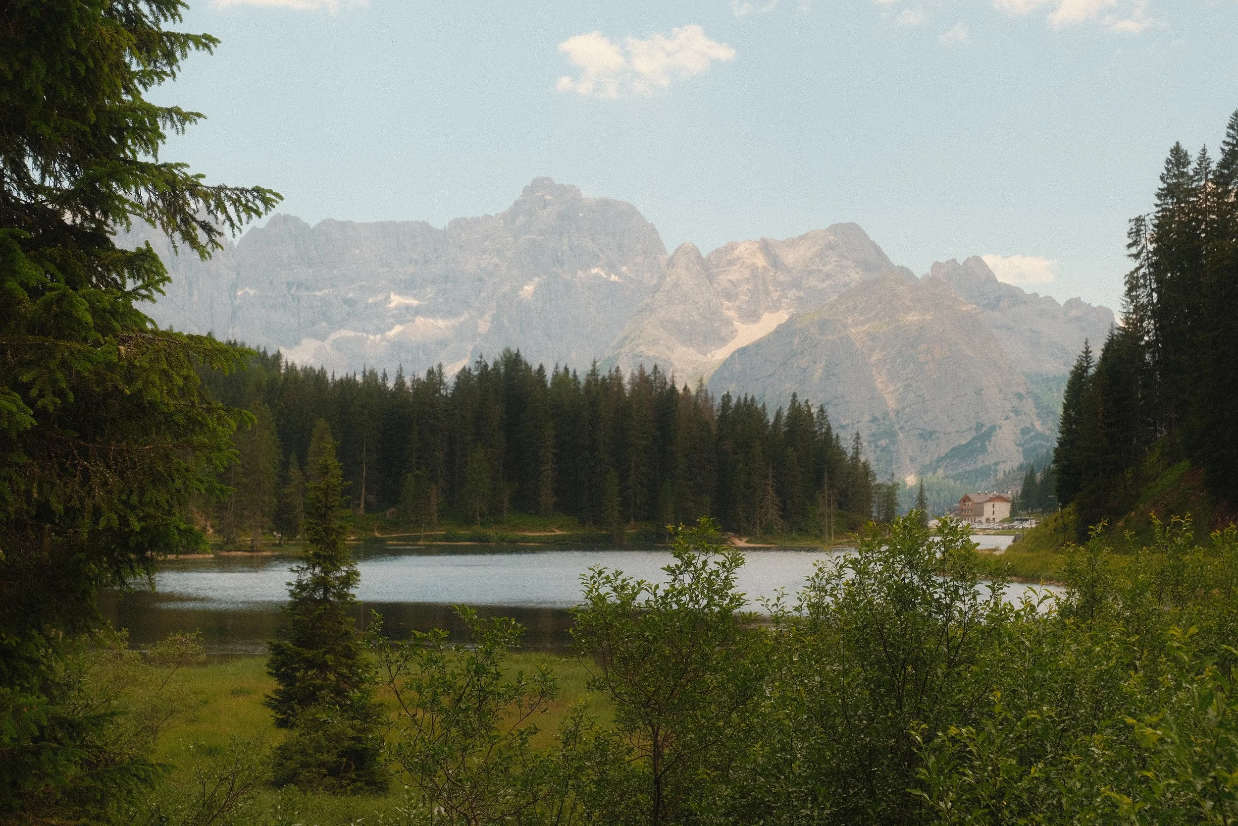 Scenic view of mountains in the distance, trees in the foreground, a river or lake at the base of the mountains, and a few small buildings near the water.