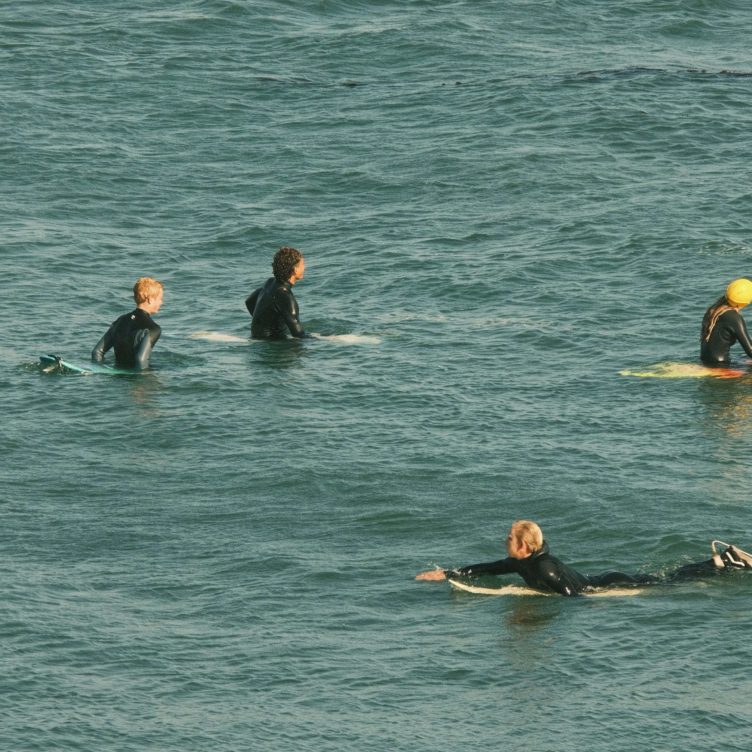 People in wetsuits at the beach, some on surfboards, with the ocean extending into the distance.