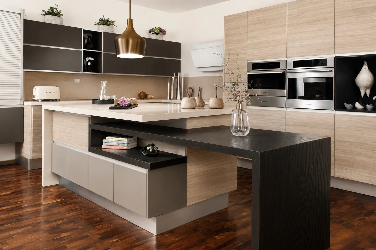 Modern kitchen with light wood cabinets, stainless steel appliances, black and beige accents, a white and black island, and decorative items including vases and plants.