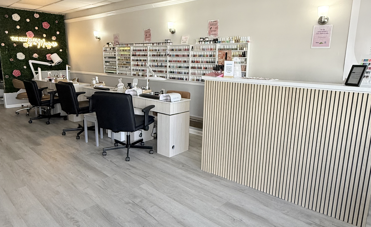 Nail salon with four manicure stations, shelves of nail polish bottles, and a reception desk.