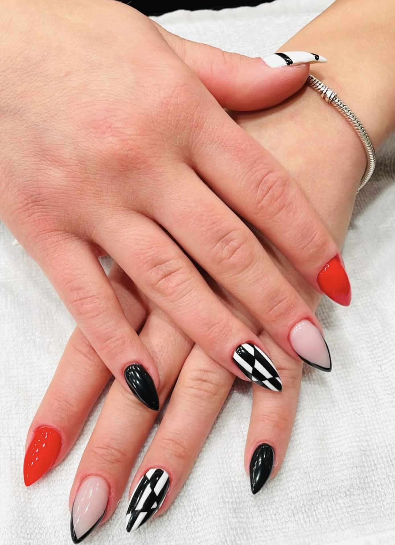 Close-up of hands with manicured nails in various designs and colors, including black, red, nude, and black-and-white geometric patterns.