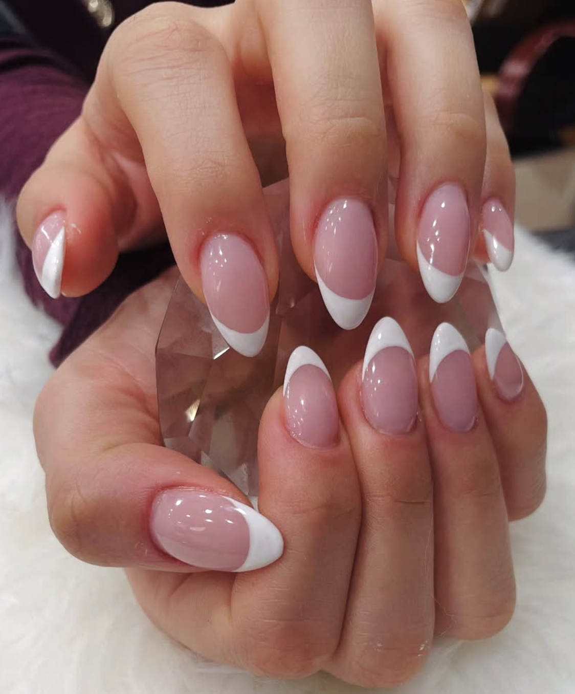 Close-up of hands with manicured nails featuring a pink base with white French tips, holding a clear faceted crystal against a soft background.