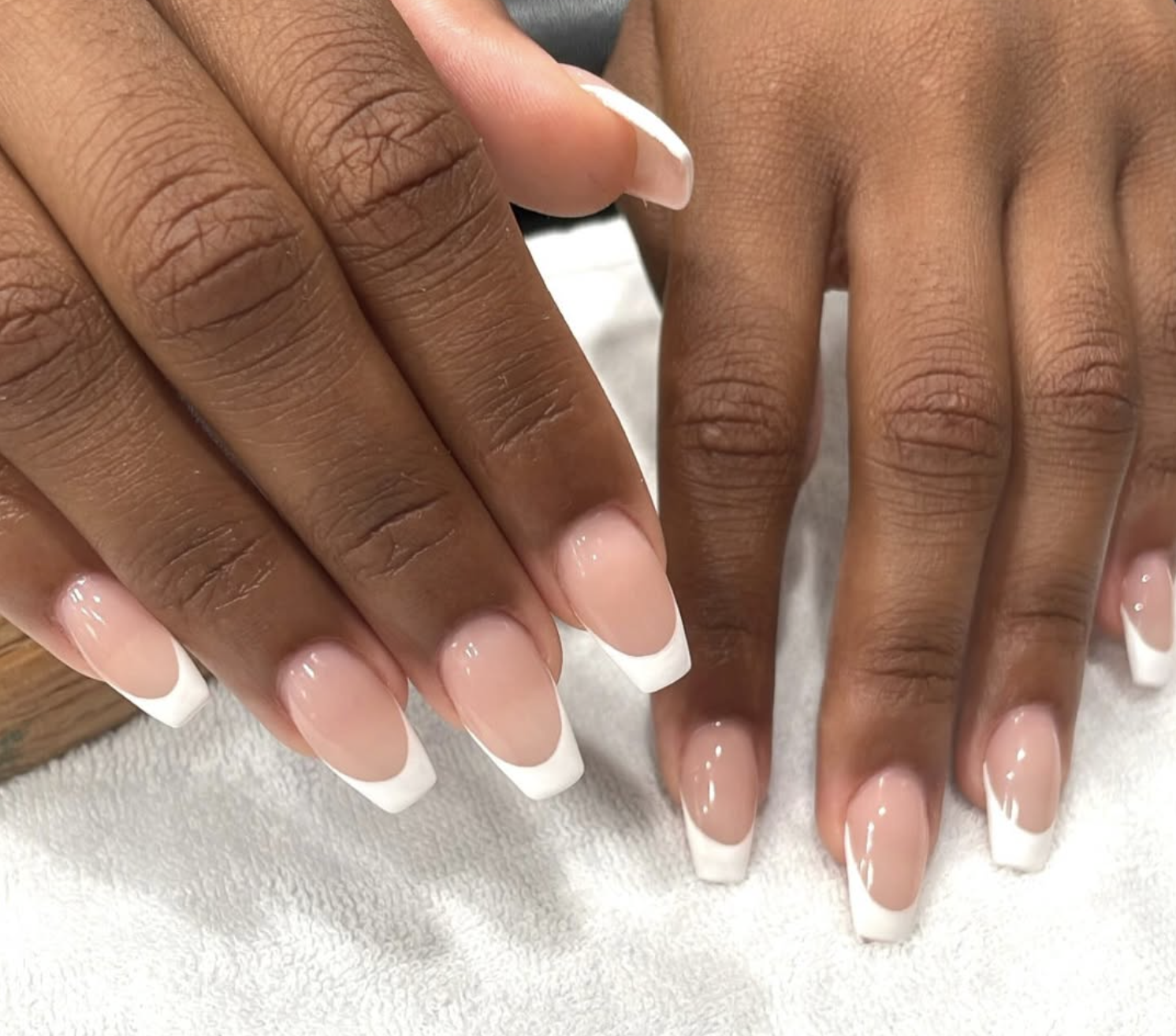Close-up of two hands resting on a white textured surface, showing manicured nails with French tips.