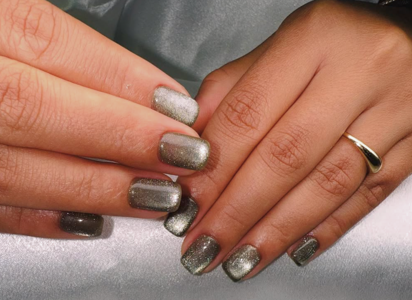 Close-up of two hands with silver glittery nail polish, one hand wearing a gold ring on the ring finger.