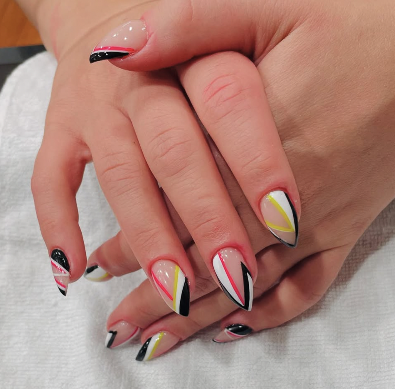 Close-up of hands with colorful geometric patterned manicure, featuring black, white, pink, yellow, and red lines and shapes.