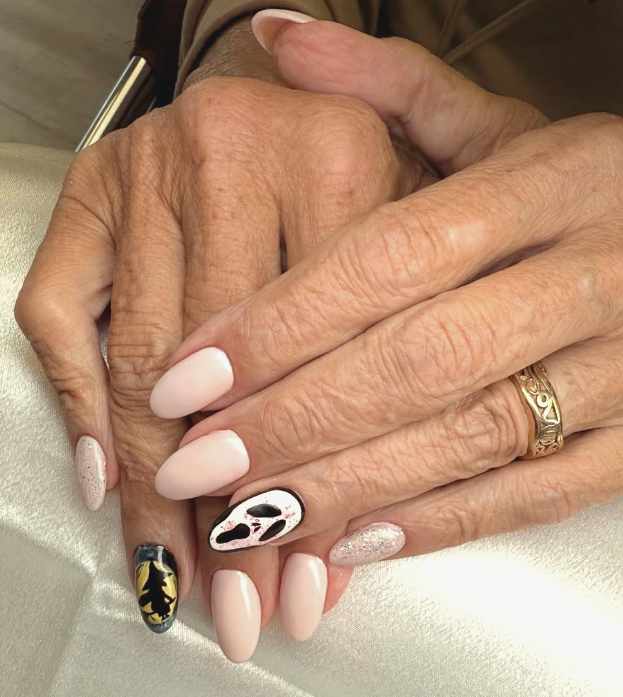 Close-up of two hands with manicured fingernails, resting together. The nails are painted in neutral, glittery, and artistic designs, including a leopard pattern, floral motifs, and abstract art.
