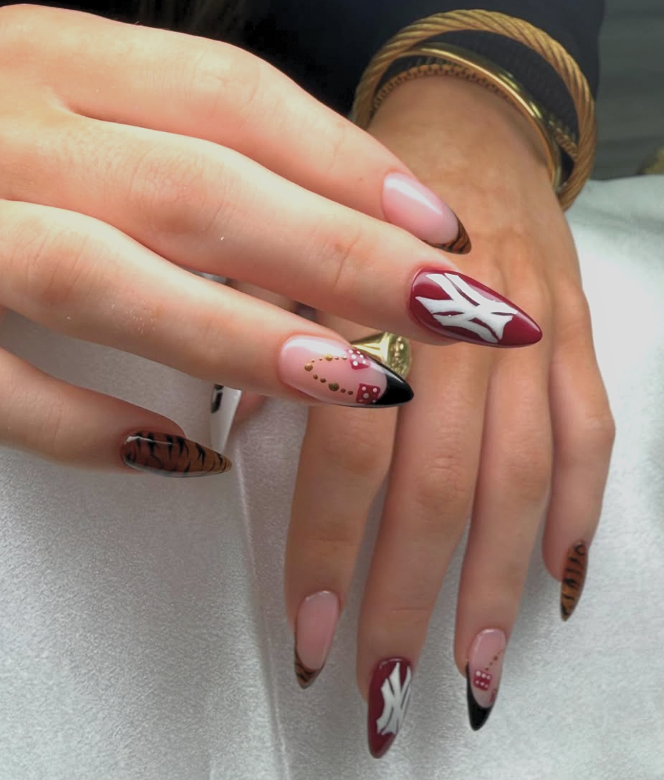 Close-up of a woman's hand showing manicured nails with creative and colorful designs, including animal print, abstract patterns, and decorative accents.