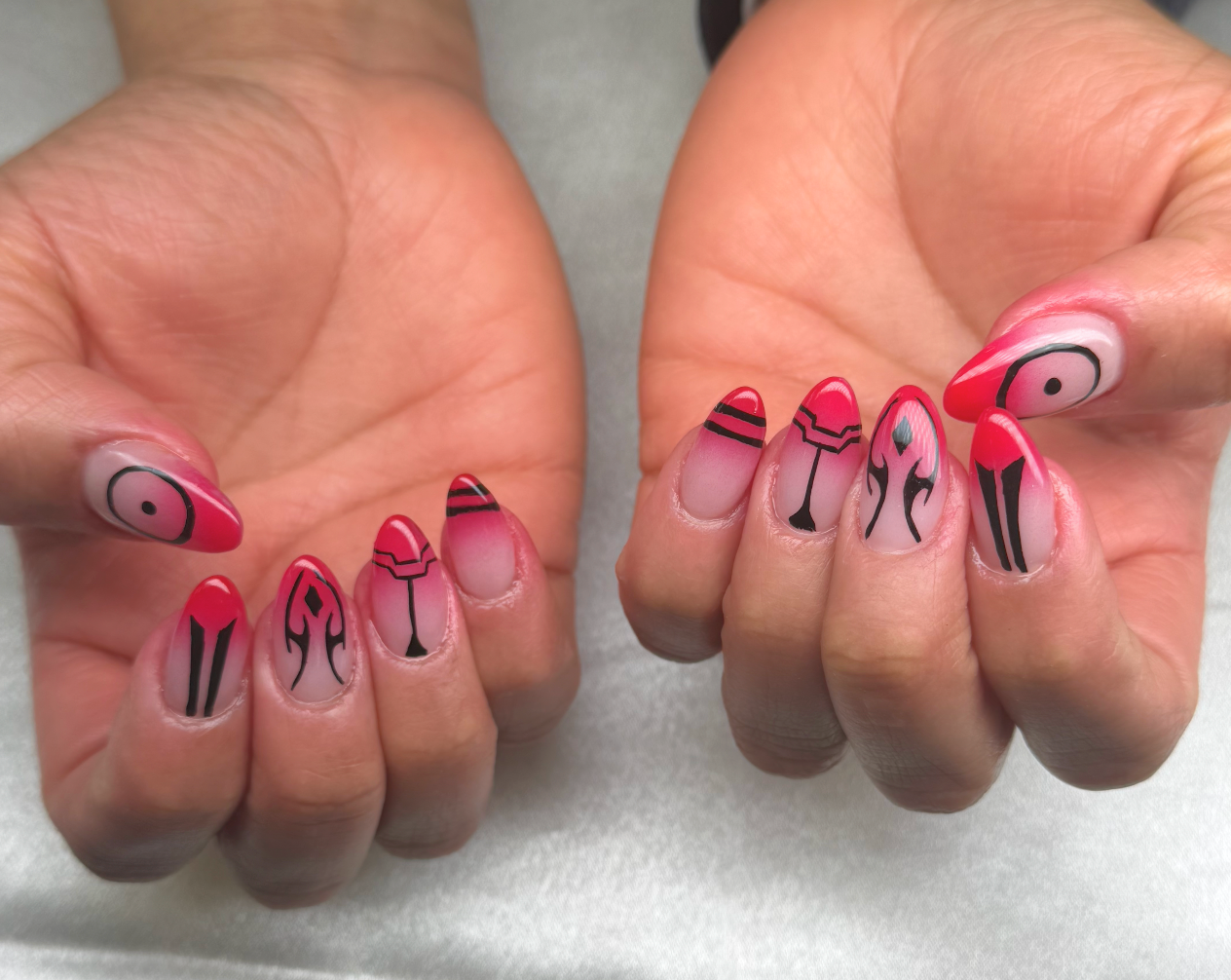Nail art with red and black designs inspired by tribal and abstract patterns on long, almond-shaped nails.
