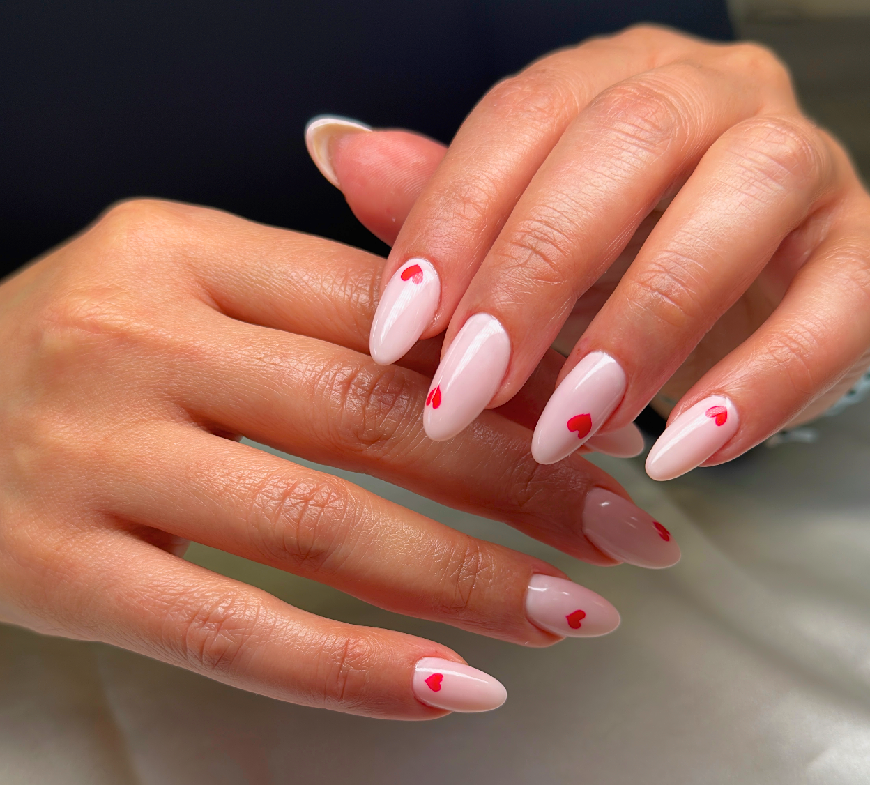 Close-up of hands with manicured nails painted in pale pink with small red heart designs.