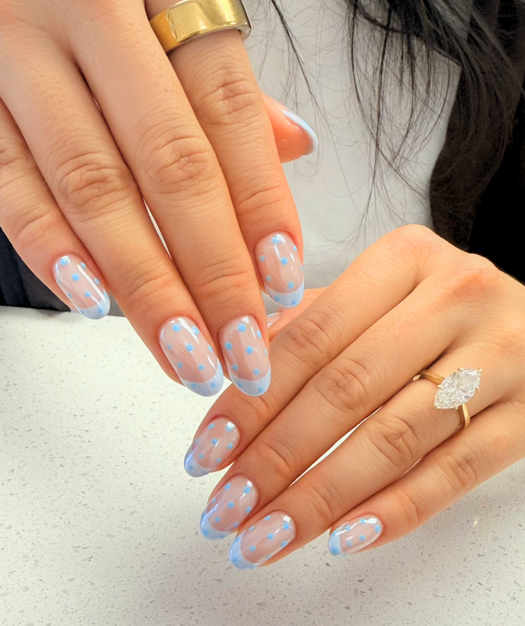 Close-up of a person's hands with manicured nails featuring a blue and white polka dot design and a large.
