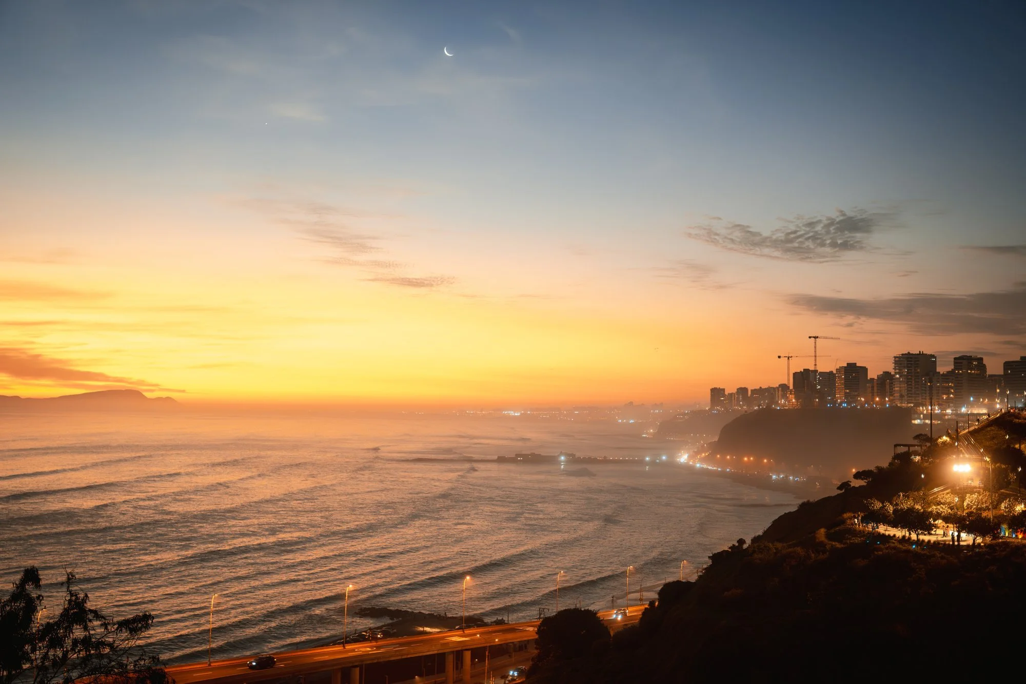 Atardecer dorado sobre la bahía de Lima con la luna creciente asomando