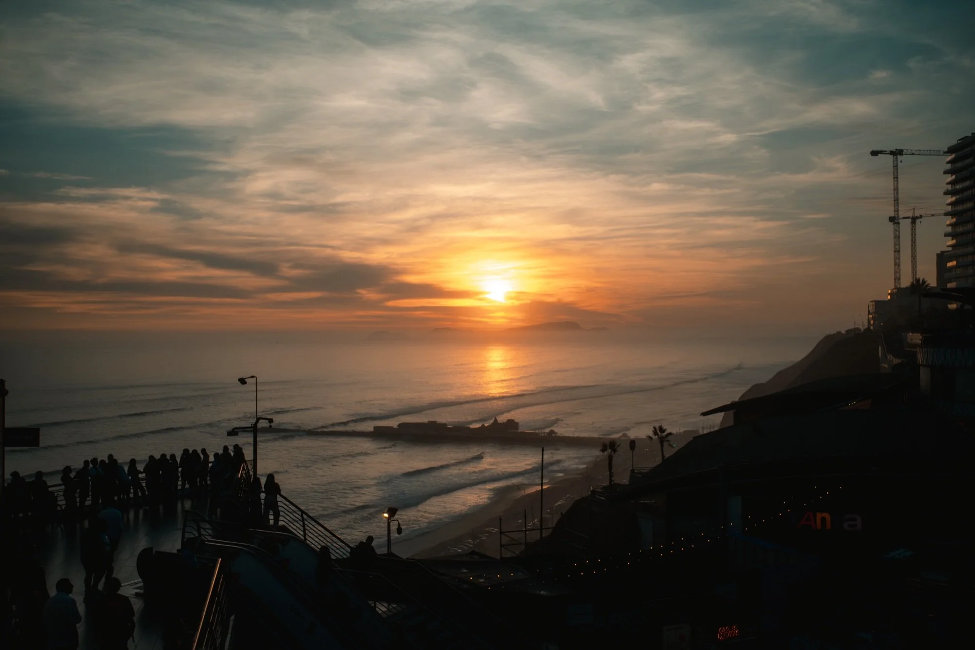 Atardecer sobre el mar con gente reunida en el malecón