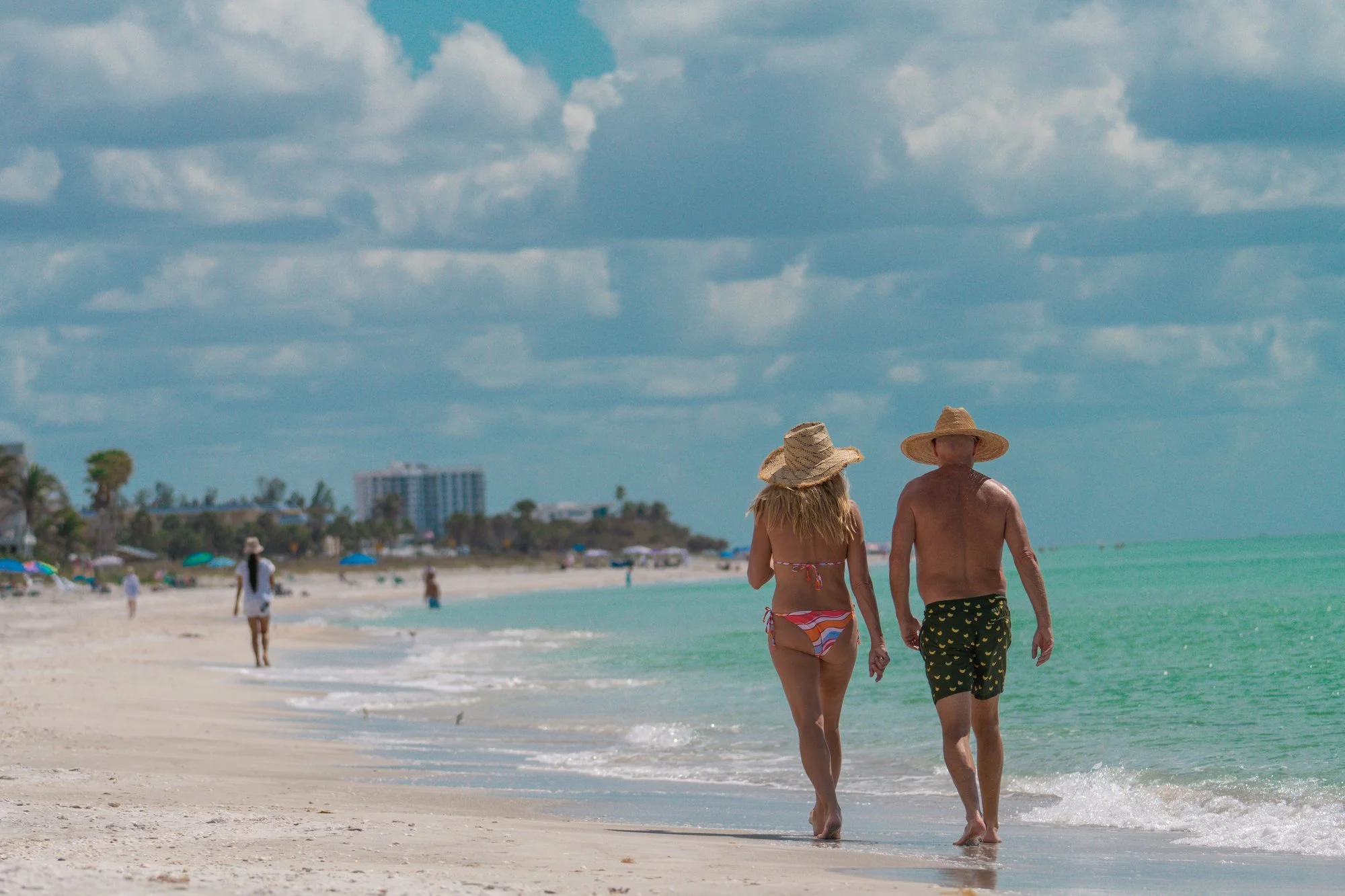 Pareja con sombreros caminando por la orilla del mar