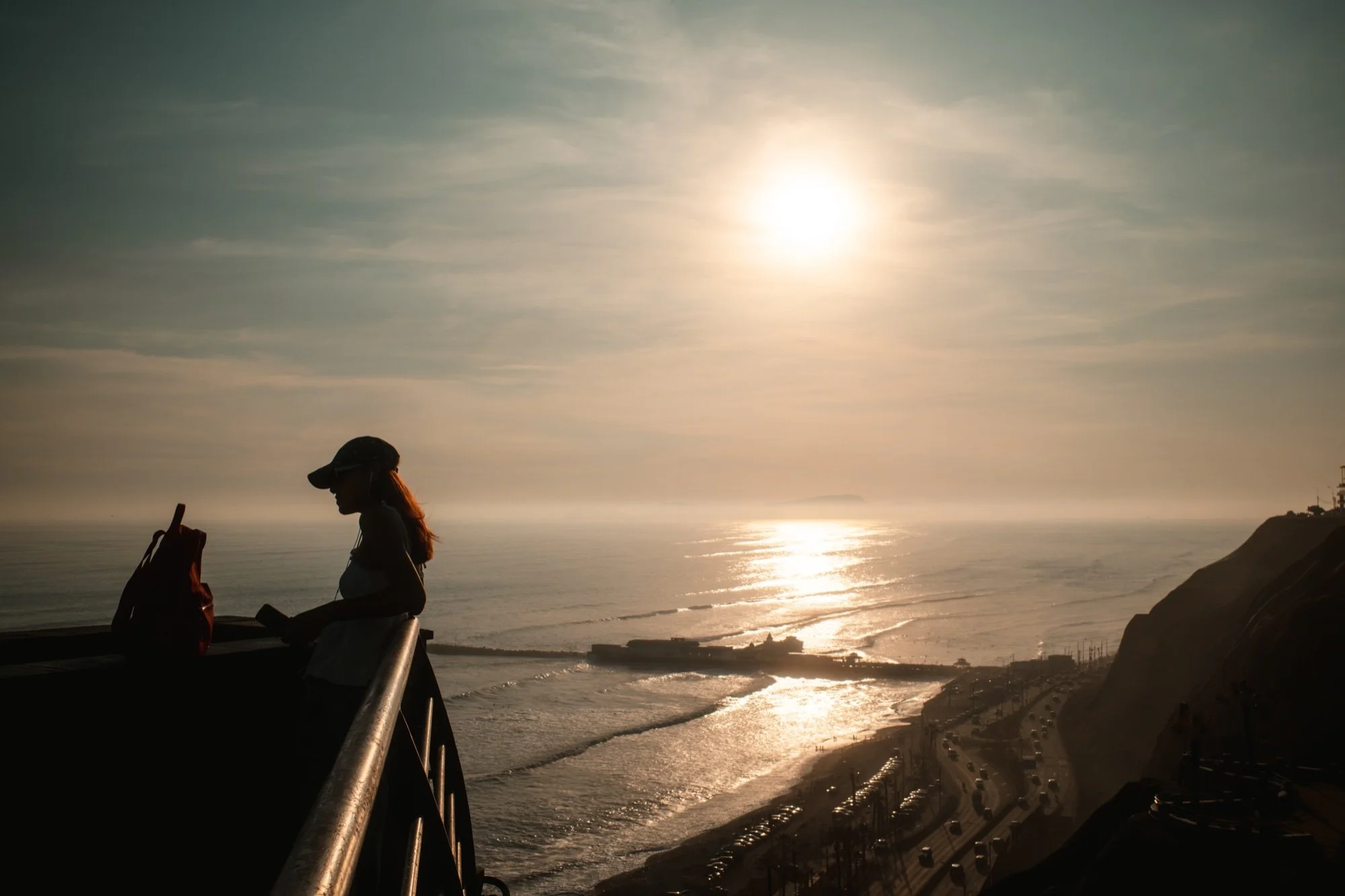 Silueta de una mujer con gorra mirando el atardecer desde la baranda