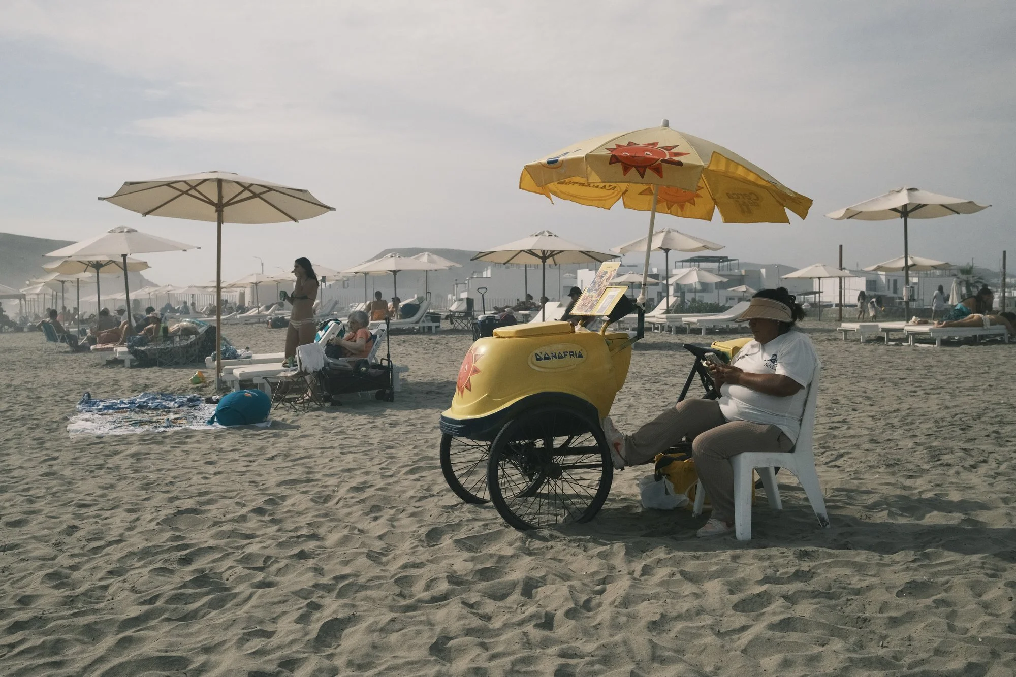 Vendedor ambulante con su carrito en una playa con sombrillas