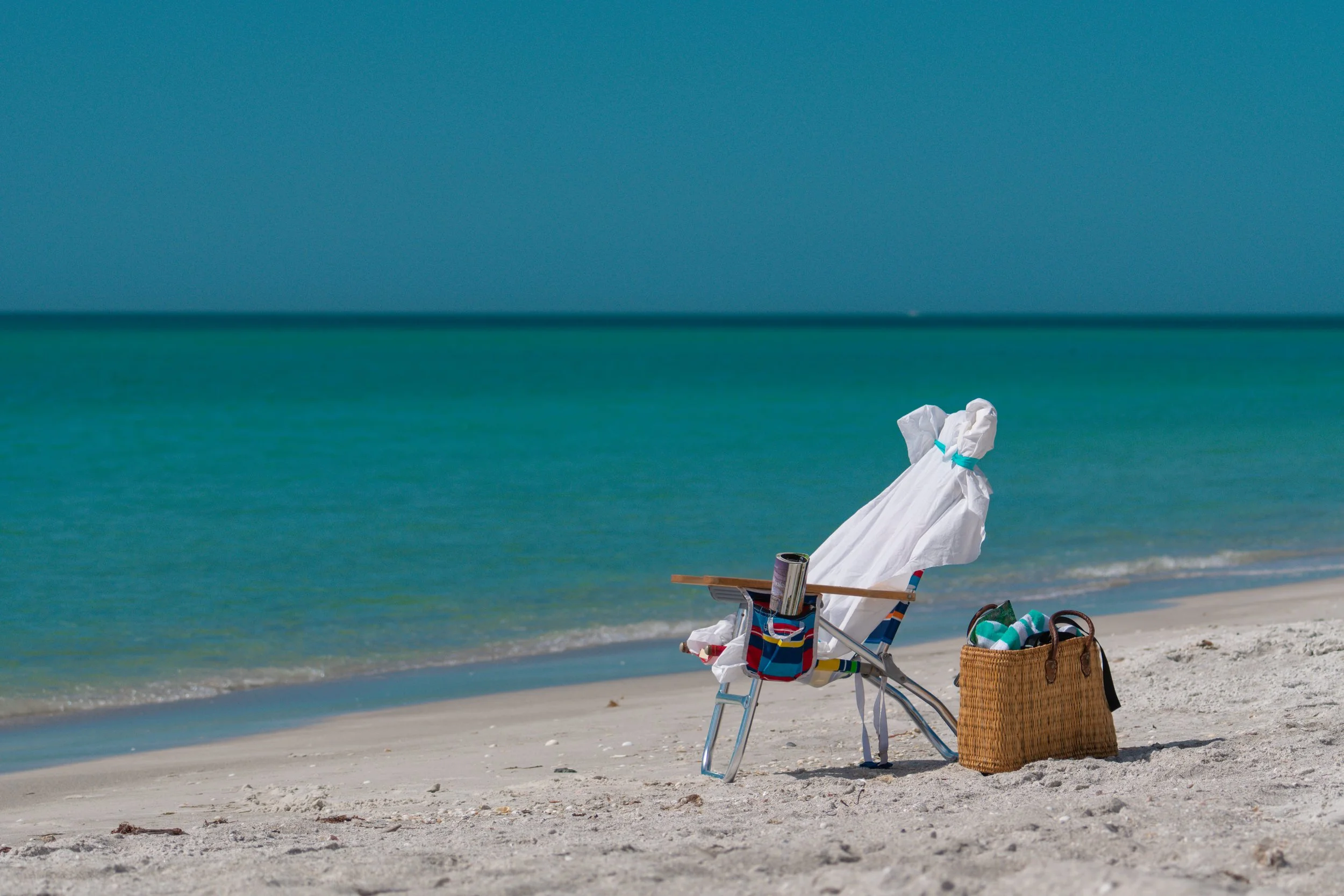 Silla de playa con una camisa blanca y un bolso sobre la arena.