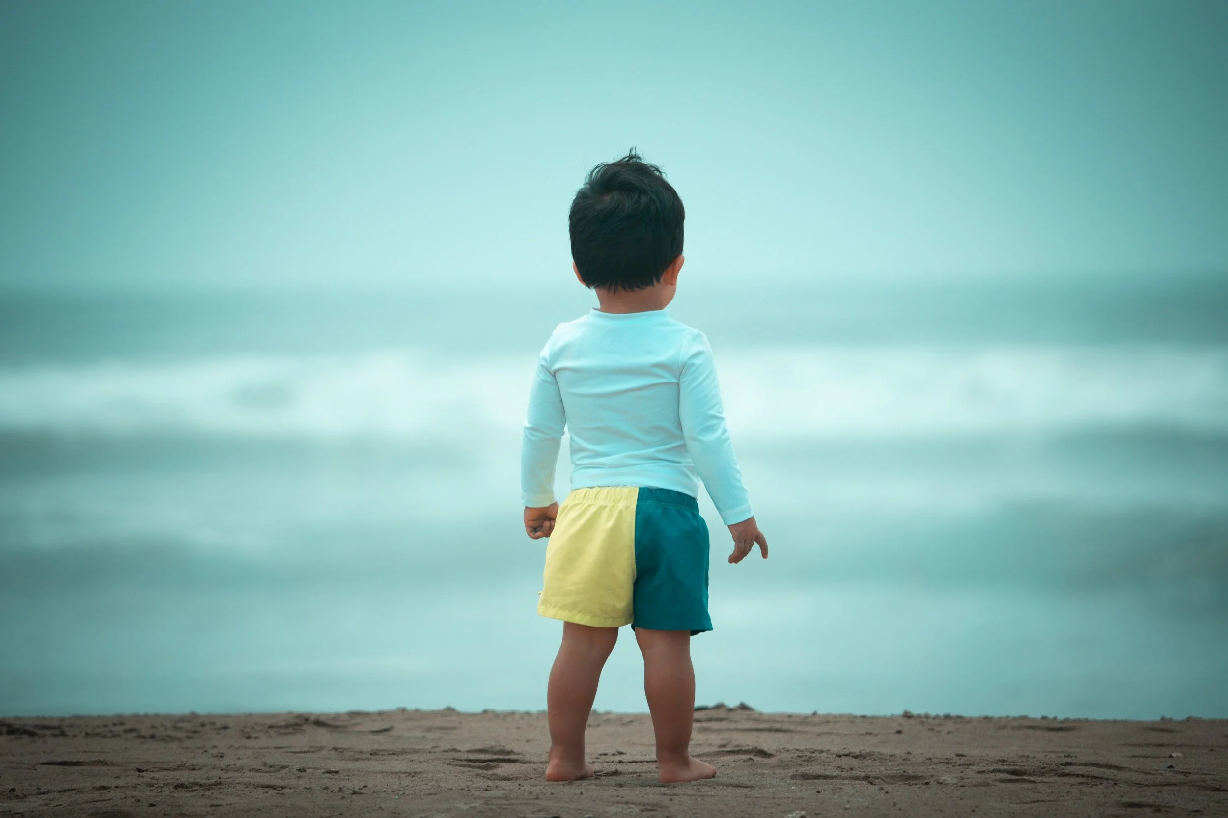 Niño de espaldas frente al mar brumoso en la playa