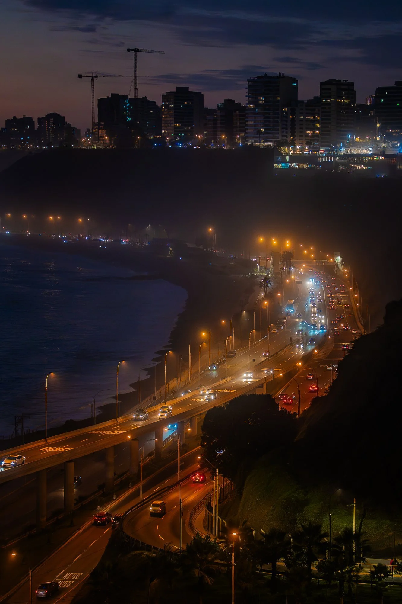 Malecón de la Costa Verde de noche con tráfico y la ciudad iluminada