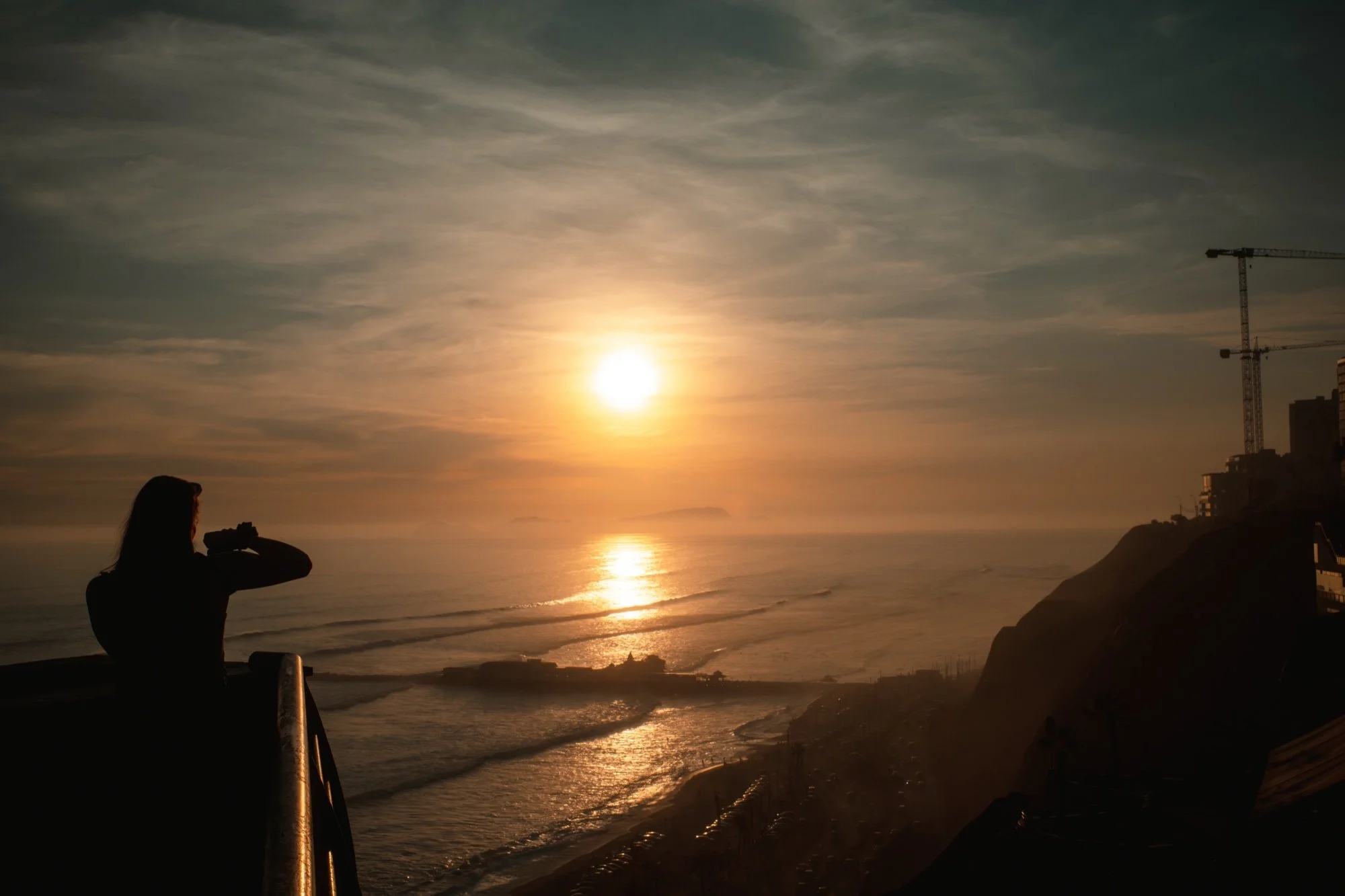 Silueta de una persona fotografiando el sol sobre el mar