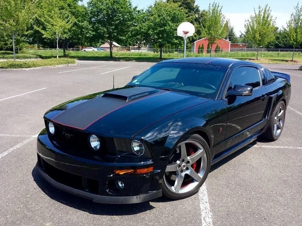 A black Ford Mustang with a hood scoop and red accents parked in an empty parking lot.