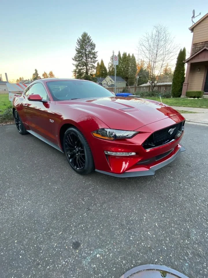 Red Ford Mustang parked on a residential street with trees and houses in the background during sunset.