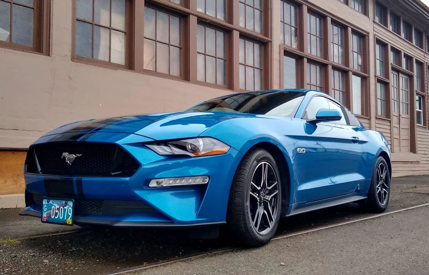 A blue Ford Mustang convertible parked on the street in front of a beige building with large windows.