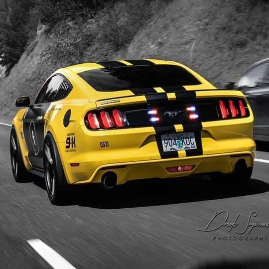 Yellow Ford Mustang police car with black racing stripes driving on a highway.