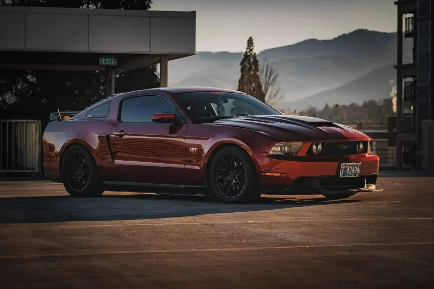 A red Ford Mustang GT parked on a rooftop parking lot at sunset with mountain scenery in the background.