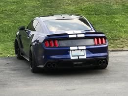 Rear view of a blue sports car parked on the grass and pavement.